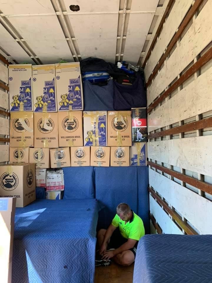 A Man is Kneeling in the Back of a Moving Truck Filled With Boxes — Wide Bay Removals In Dundowran, QLD