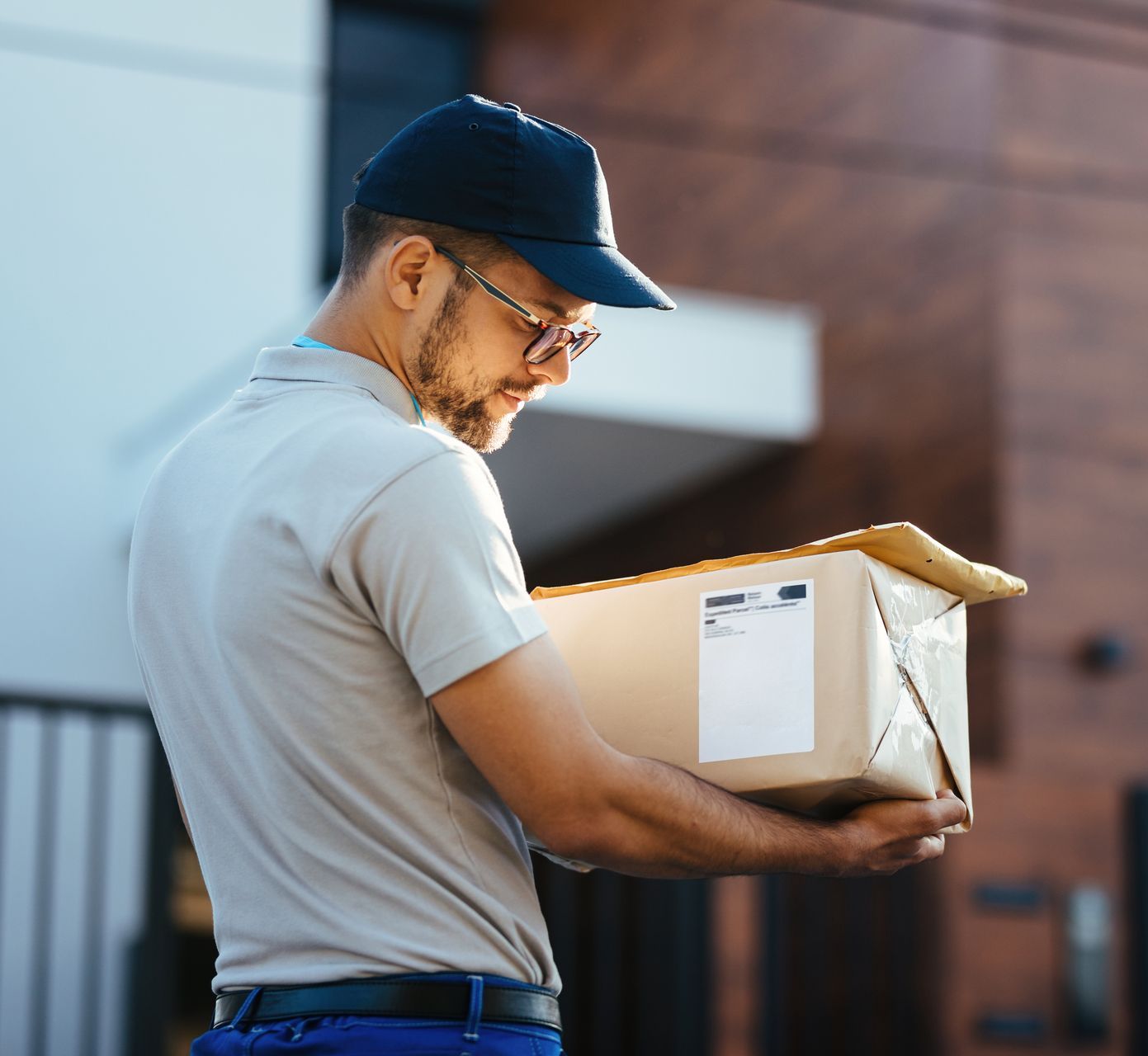 Delivery person holding a cardboard box outside a building.