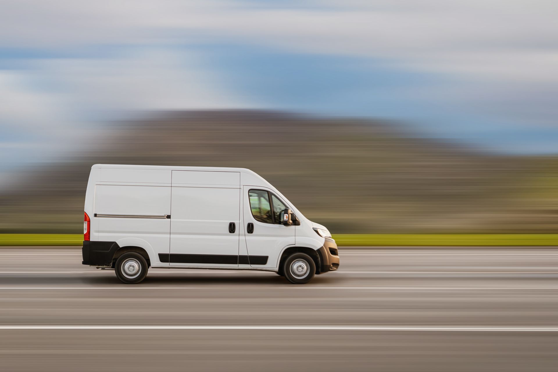 White cargo van speeding on highway, blurred background.