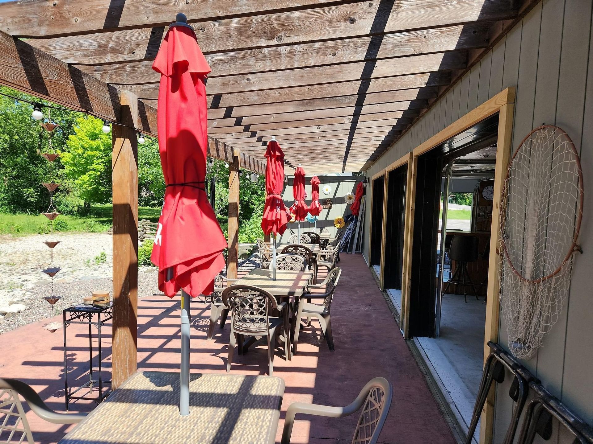 Tables and chairs under a pergola with red umbrellas