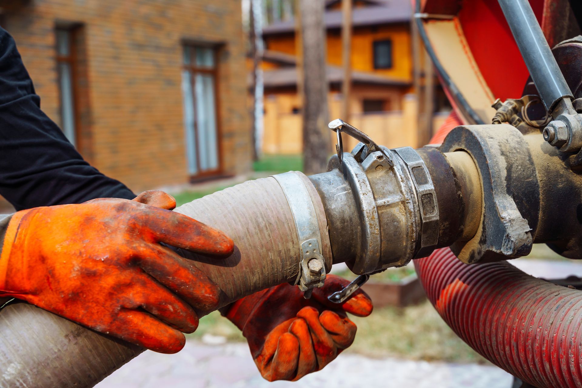 A man wearing orange gloves is connecting a hose to a pipe.