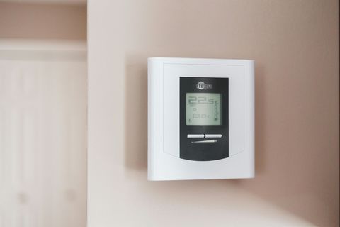 A white digital thermostat mounted on a tan wall.
