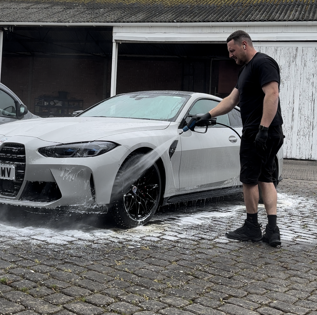 A man is washing a white car with a high pressure washer.
