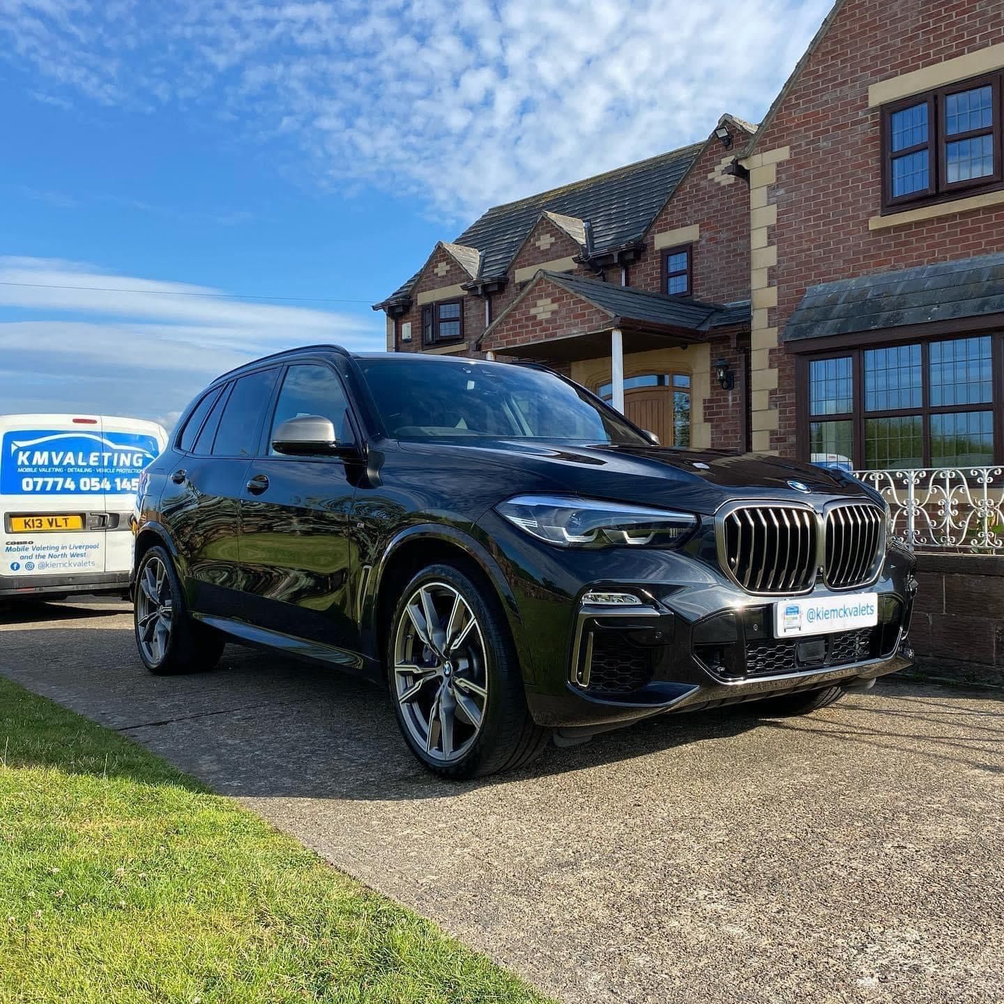 A black bmw x5 is parked in front of a brick house.