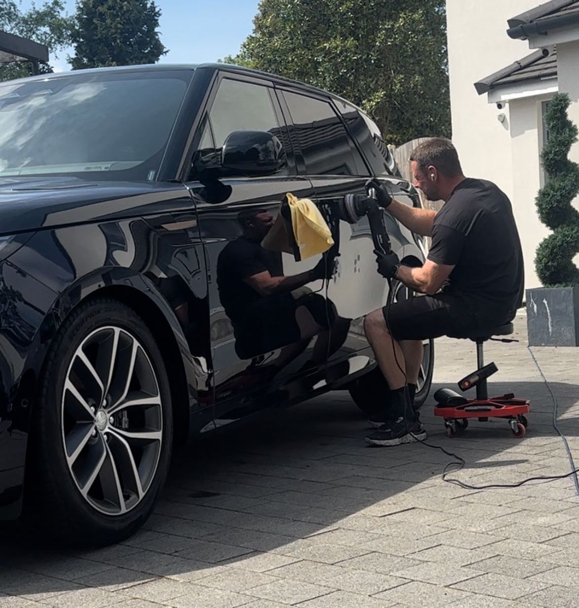 A man is sitting on a stool polishing a car.