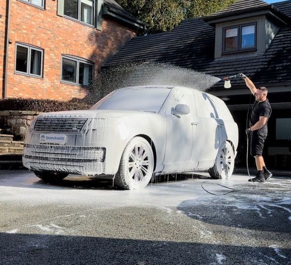 A man is washing a car with foam in front of a house.