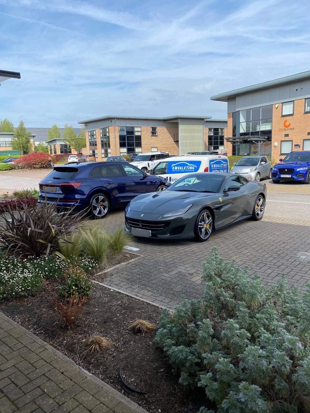 A group of cars are parked in a parking lot in front of a building.