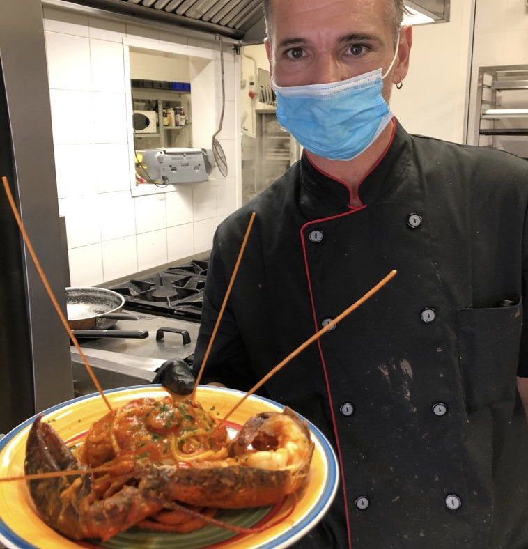 Uno chef che indossa una maschera tiene in mano un piatto di cibo