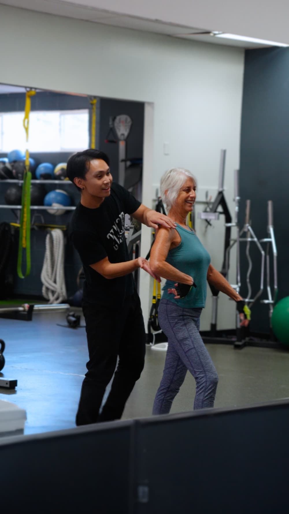 An instructor assists a person exercising in a gym. The person is using weights.