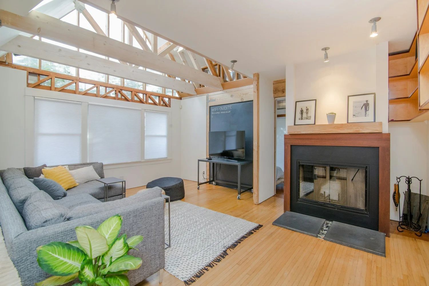 Bright living room with gray sofa, fireplace, TV, and wood beams, lit by natural light.