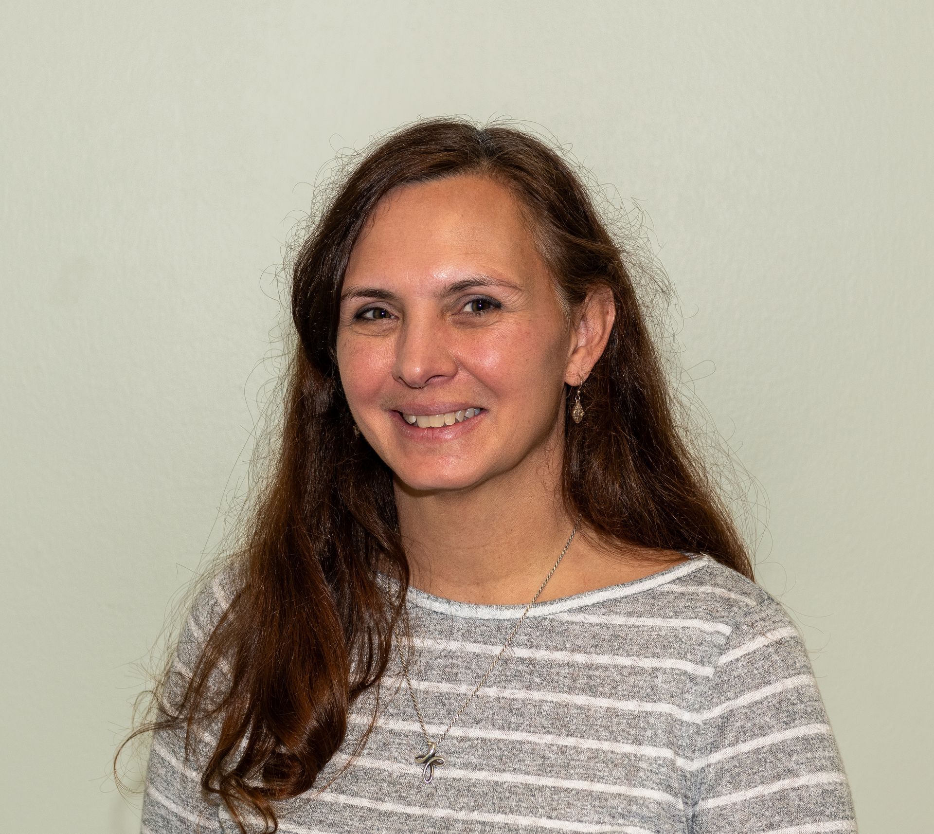 A woman in a white shirt and hoop earrings is looking at the camera with her arms crossed.