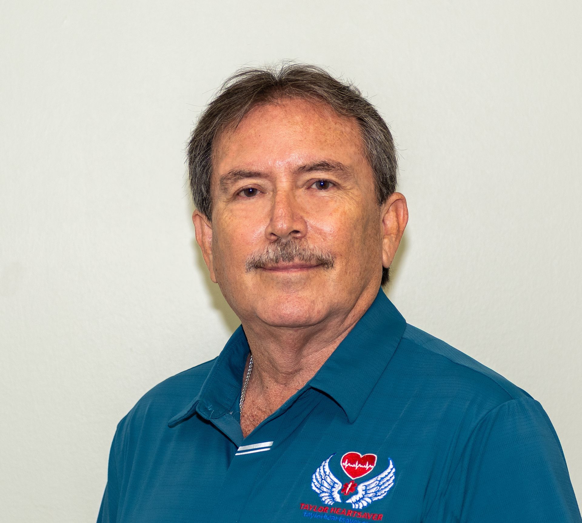 A man with a mustache is wearing a blue shirt with a heart and wings on it.