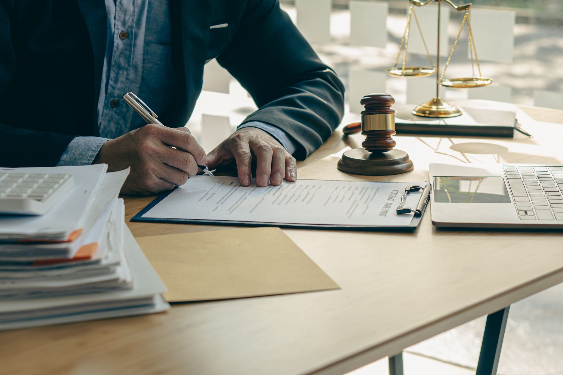 Hand signing a document at a desk with a gavel and papers nearby