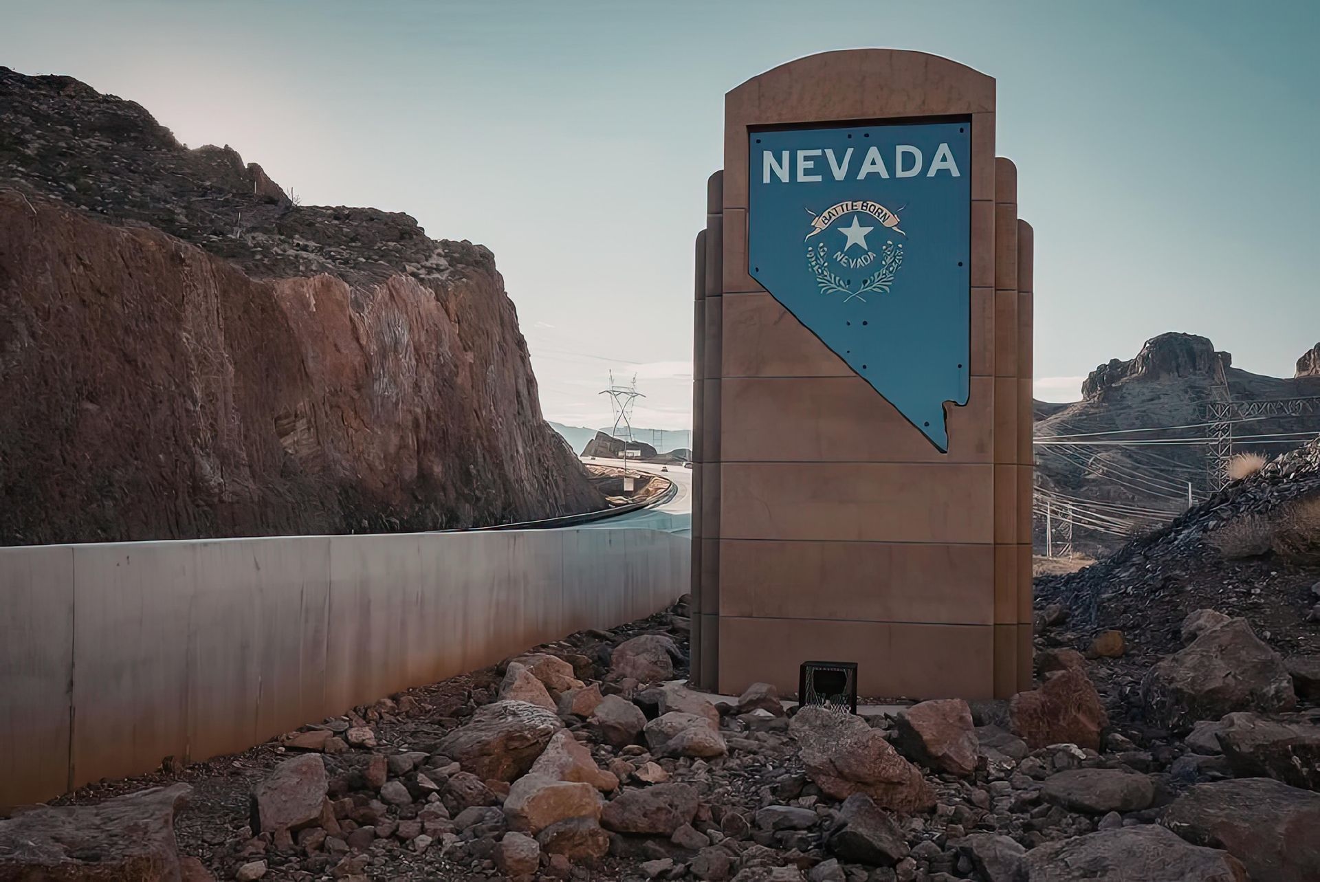 Nevada state sign beside a highway, framed by rocky canyon walls and a concrete barrier.
