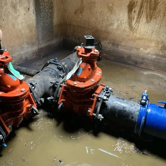 A person is working on a water pipe in a muddy room.