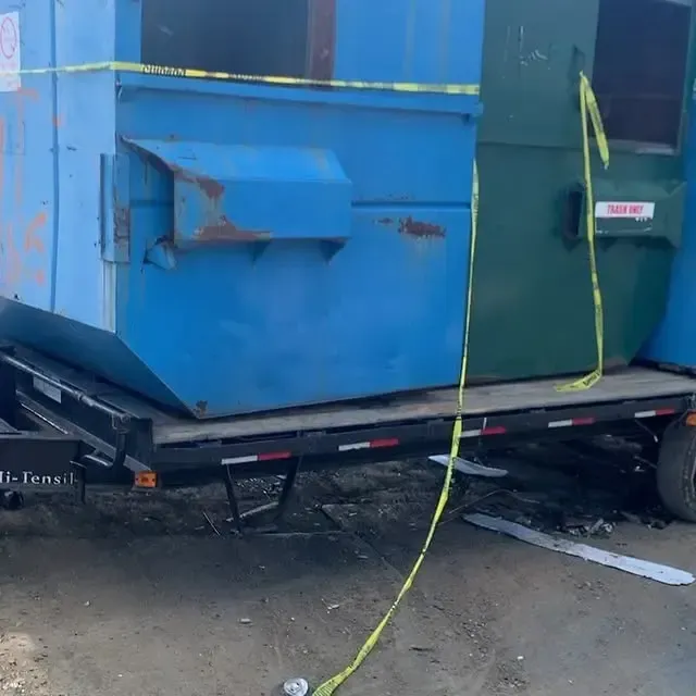 A blue dumpster is sitting on top of a trailer.