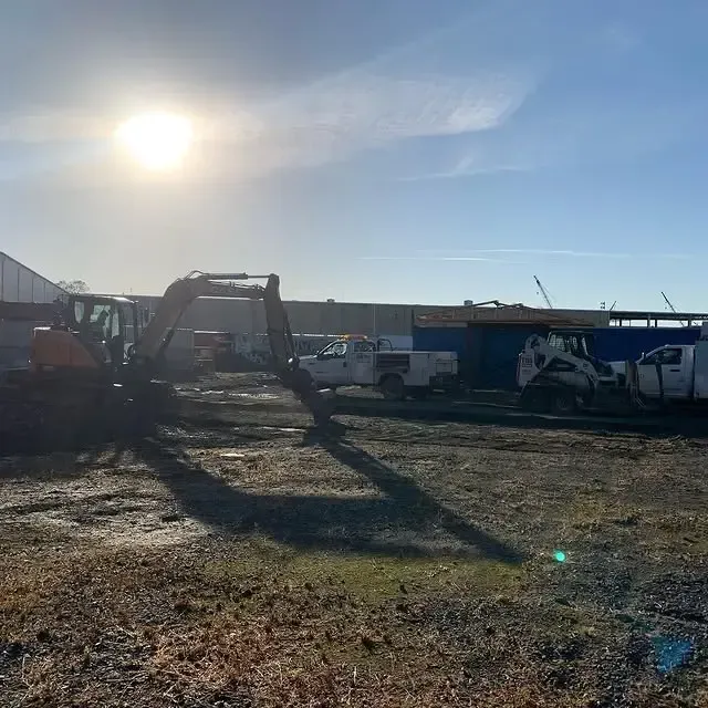 A group of construction vehicles are parked in a dirt lot in front of a building.