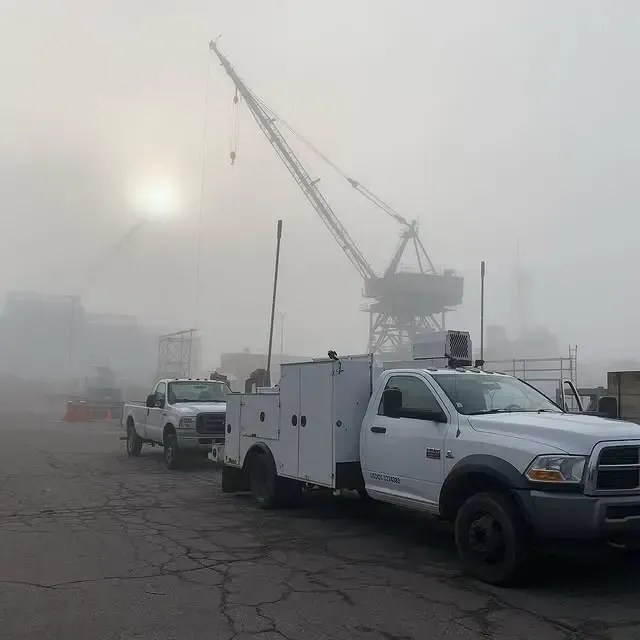 Two trucks are parked in a foggy parking lot with a crane in the background.