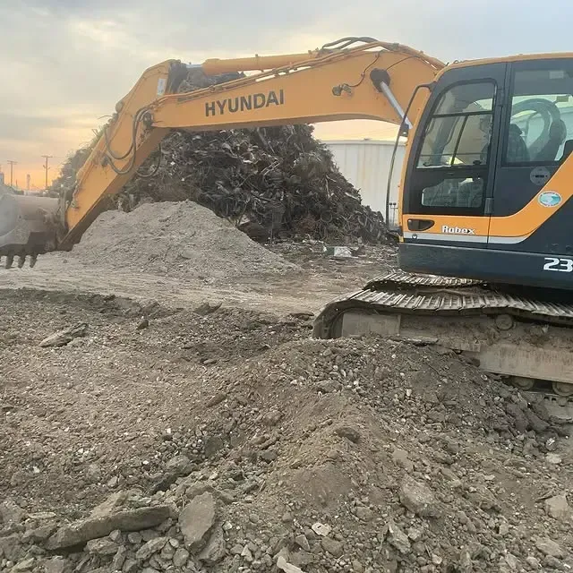 A yellow hyundai excavator is digging in a pile of dirt
