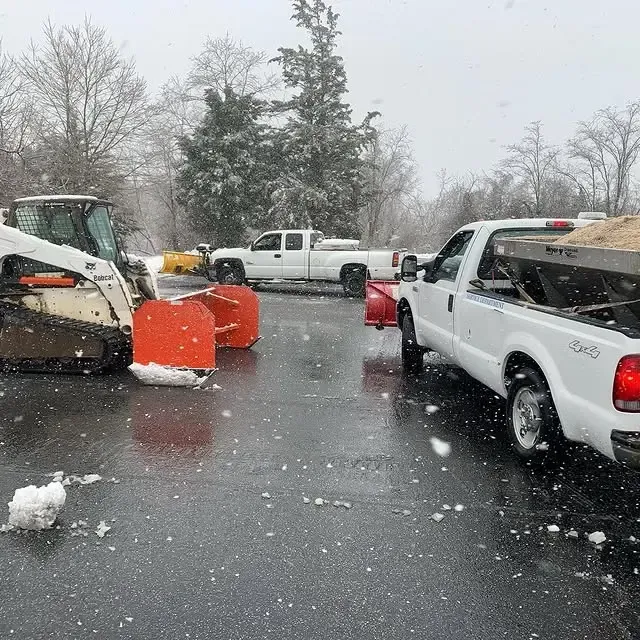 A white truck is parked next to a snow plow in a parking lot.