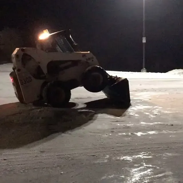 A skid steer is driving through the snow at night
