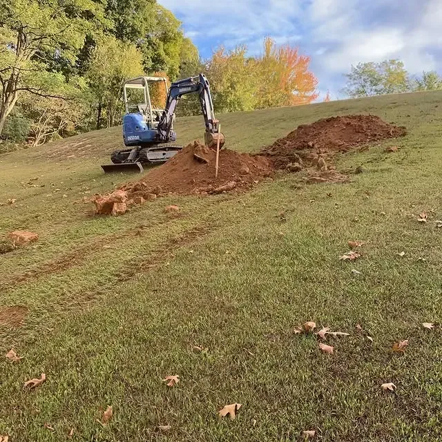 A small excavator is digging a hole in a grassy field.