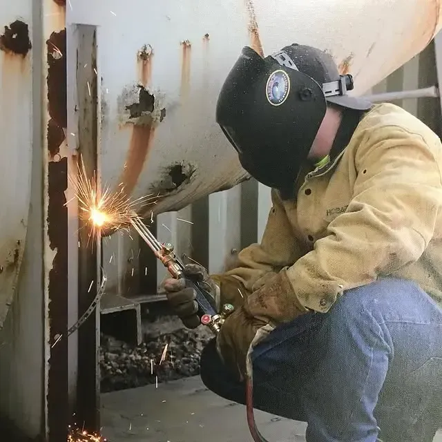 A man wearing a welding helmet is welding a piece of metal