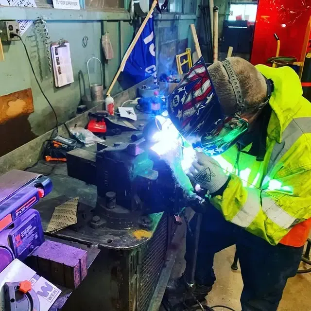 A man in a yellow jacket is welding a piece of metal