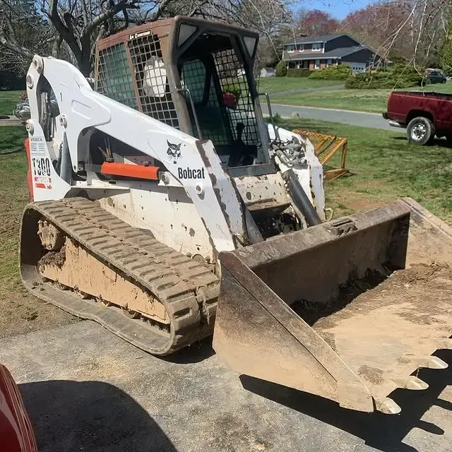 A bobcat bulldozer is parked in a driveway next to a red truck.