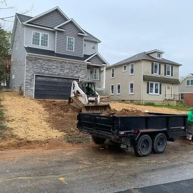 A dump truck is being loaded with dirt in front of a house.
