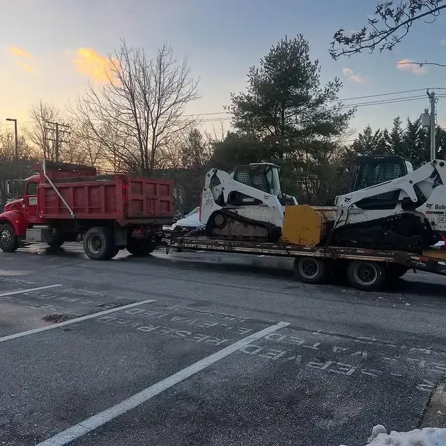 A red dump truck is towing a bulldozer on a trailer.