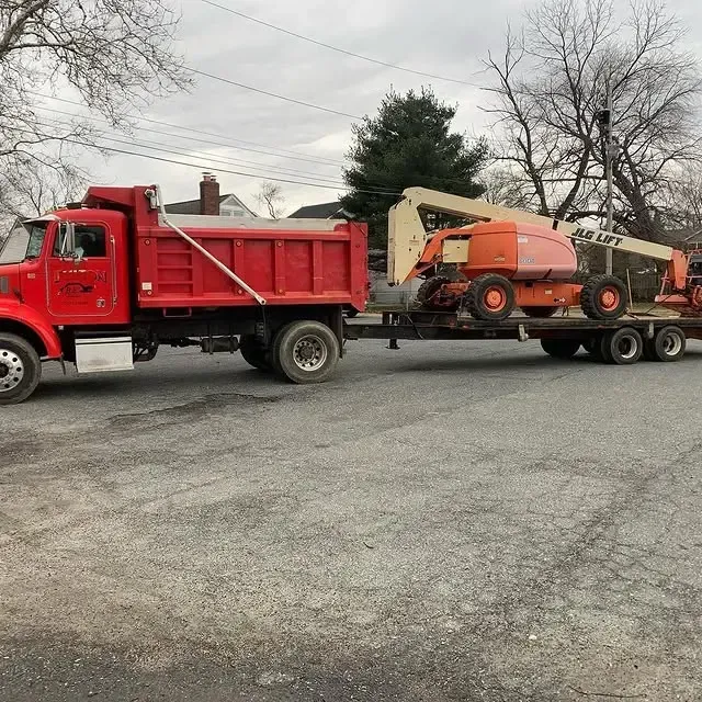 A red dump truck is carrying a lift on a trailer