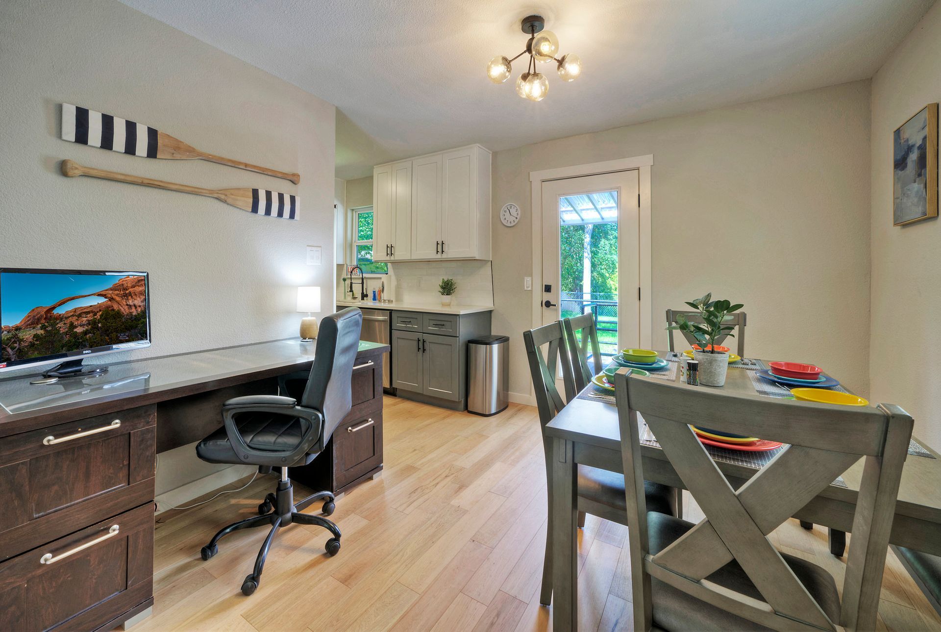 A dining room with a table and chairs and a desk with a computer on it.