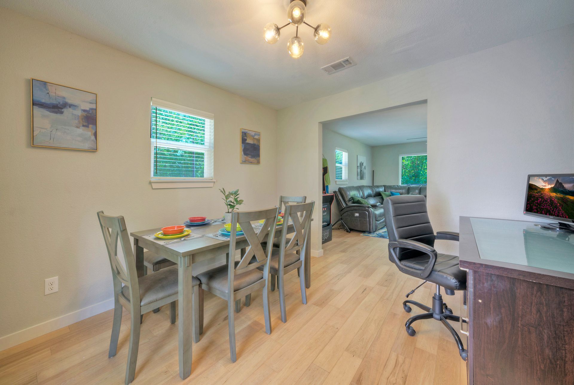 A dining room with a table and chairs and a desk with a computer on it.