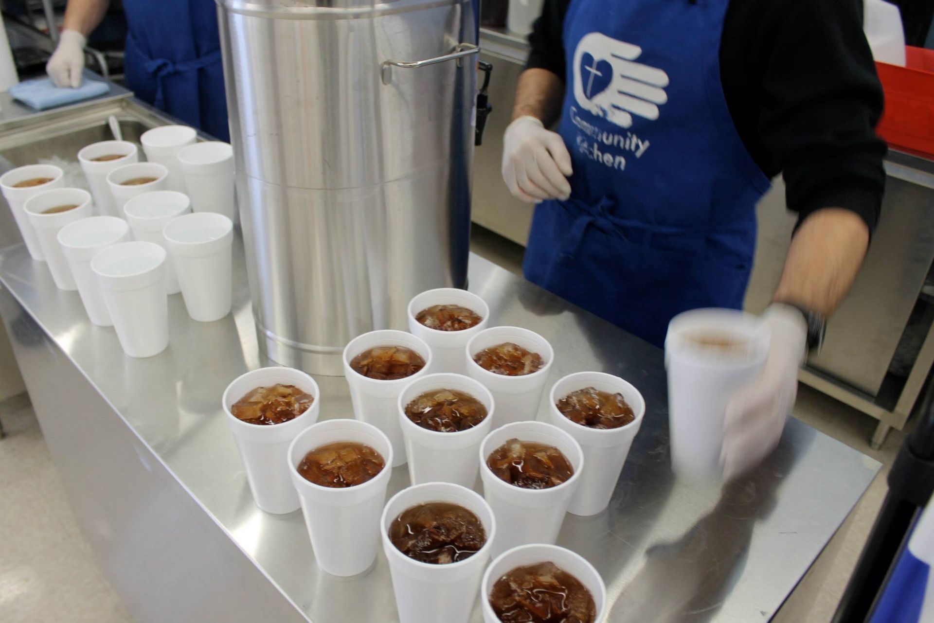 Volunteers serving drinks at Community Kitchen: pouring soda into styrofoam cups.