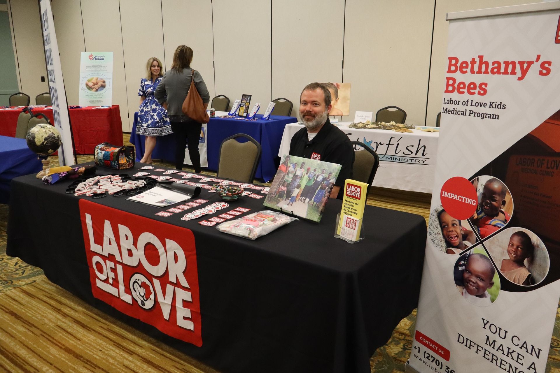 A man sits at a Labor of Love booth at an event, surrounded by marketing materials.