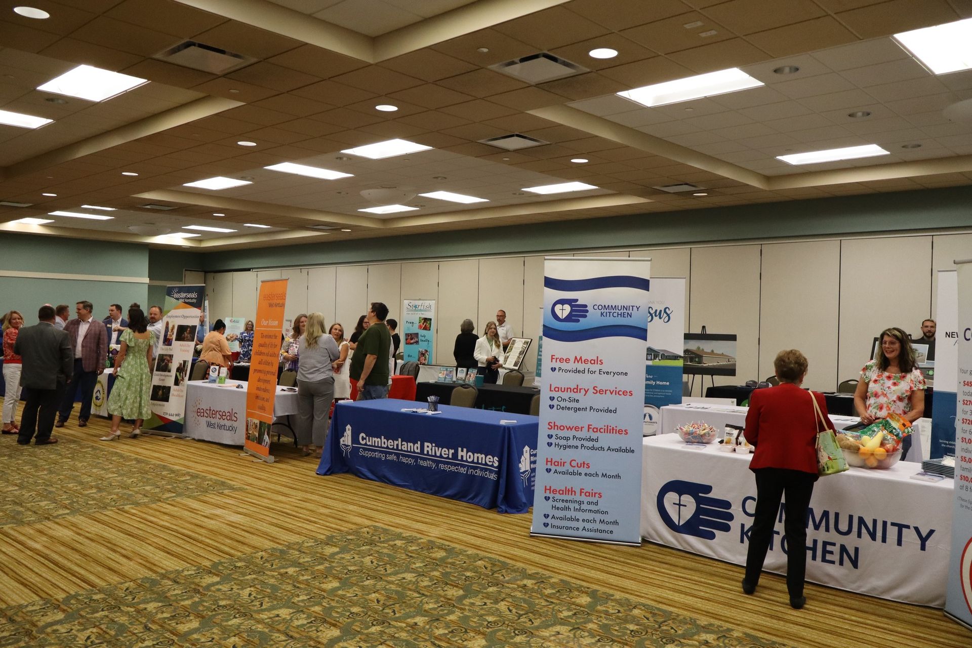 People at booths in a large convention hall. Tables with signage. Attendees interacting.