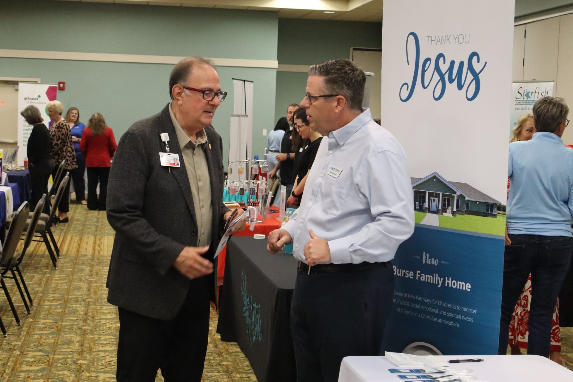 Two men talking at a booth, banner reads 