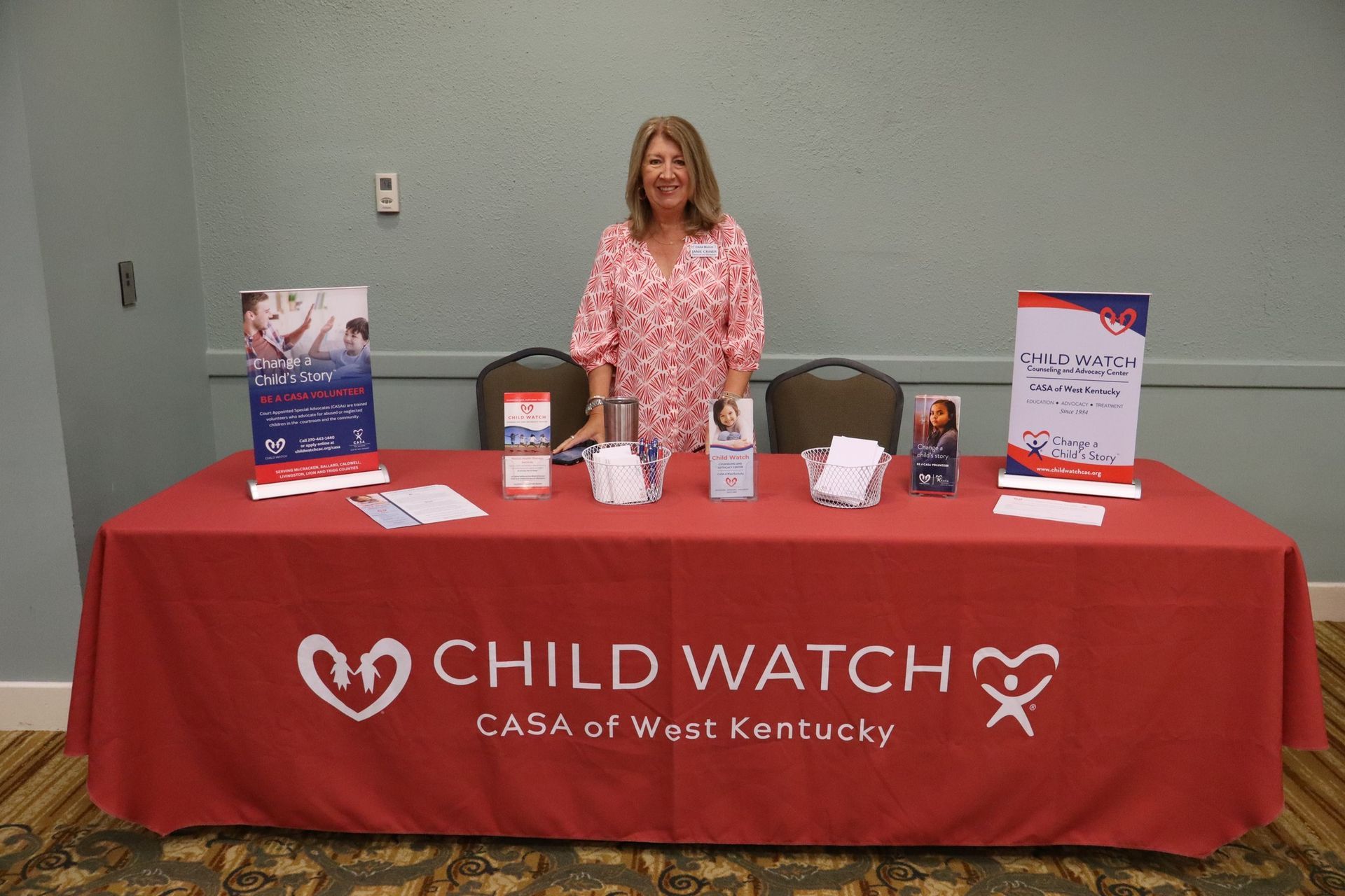 Woman at Child Watch table with brochures, red tablecloth, and CASA logo.