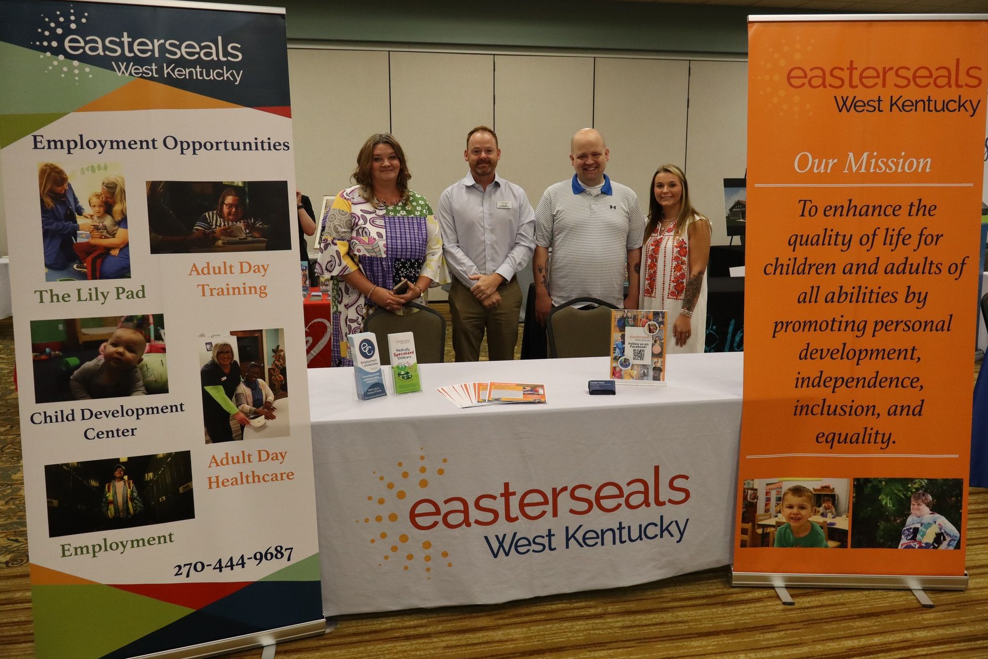Group of four people standing behind a booth with Easterseals West Kentucky banners.