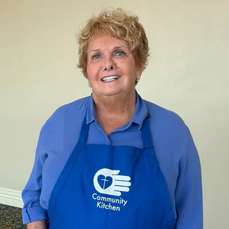 Woman in blue apron with Community Kitchen logo, smiling at the camera.
