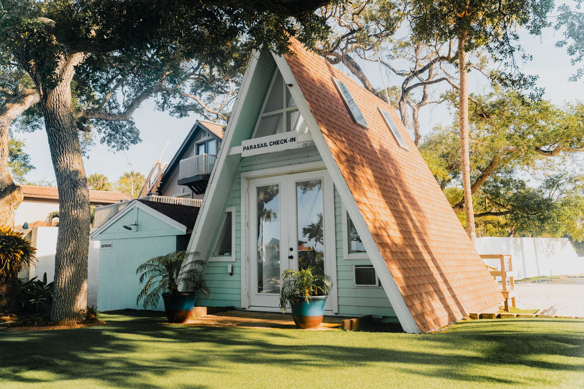 A-frame house with teal walls and brick roof, with trees and grass in the front.