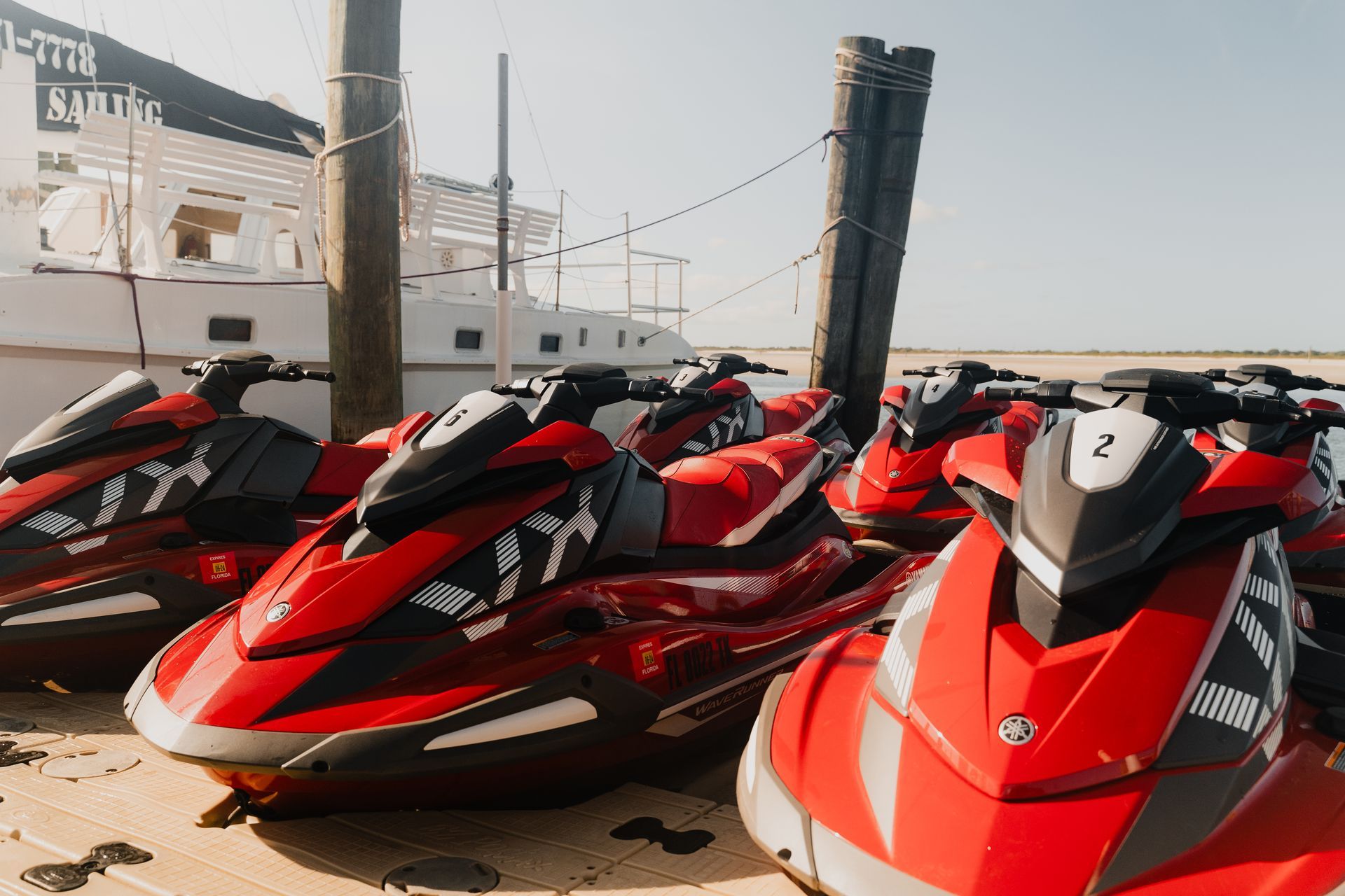 Red jet skis docked at a pier near a white building on a sunny day.