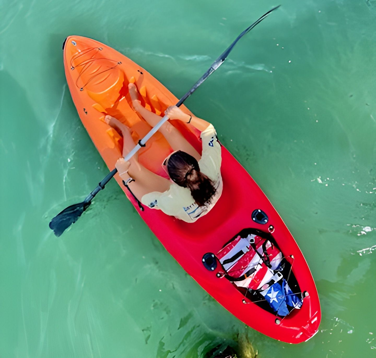 Woman kayaking in red and orange kayak, turquoise water.