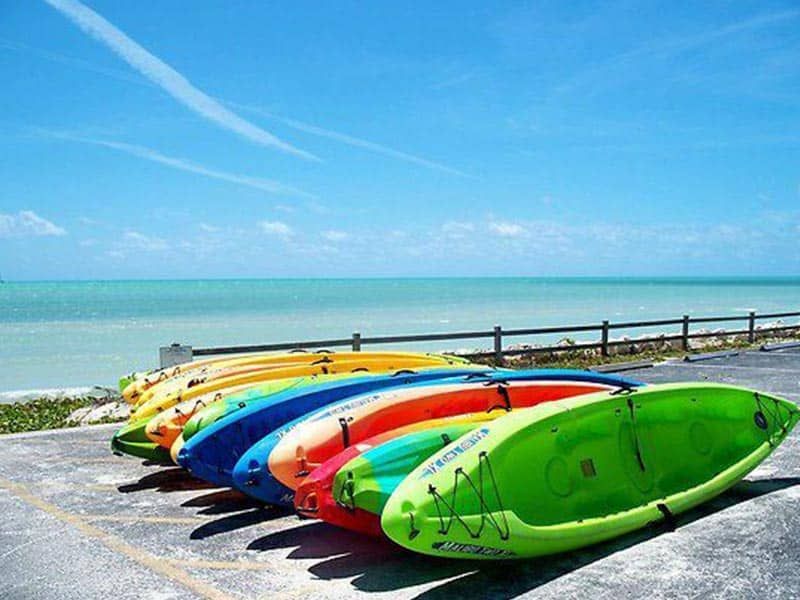 Colorful kayaks lined up on concrete, overlooking a turquoise ocean under a blue sky.