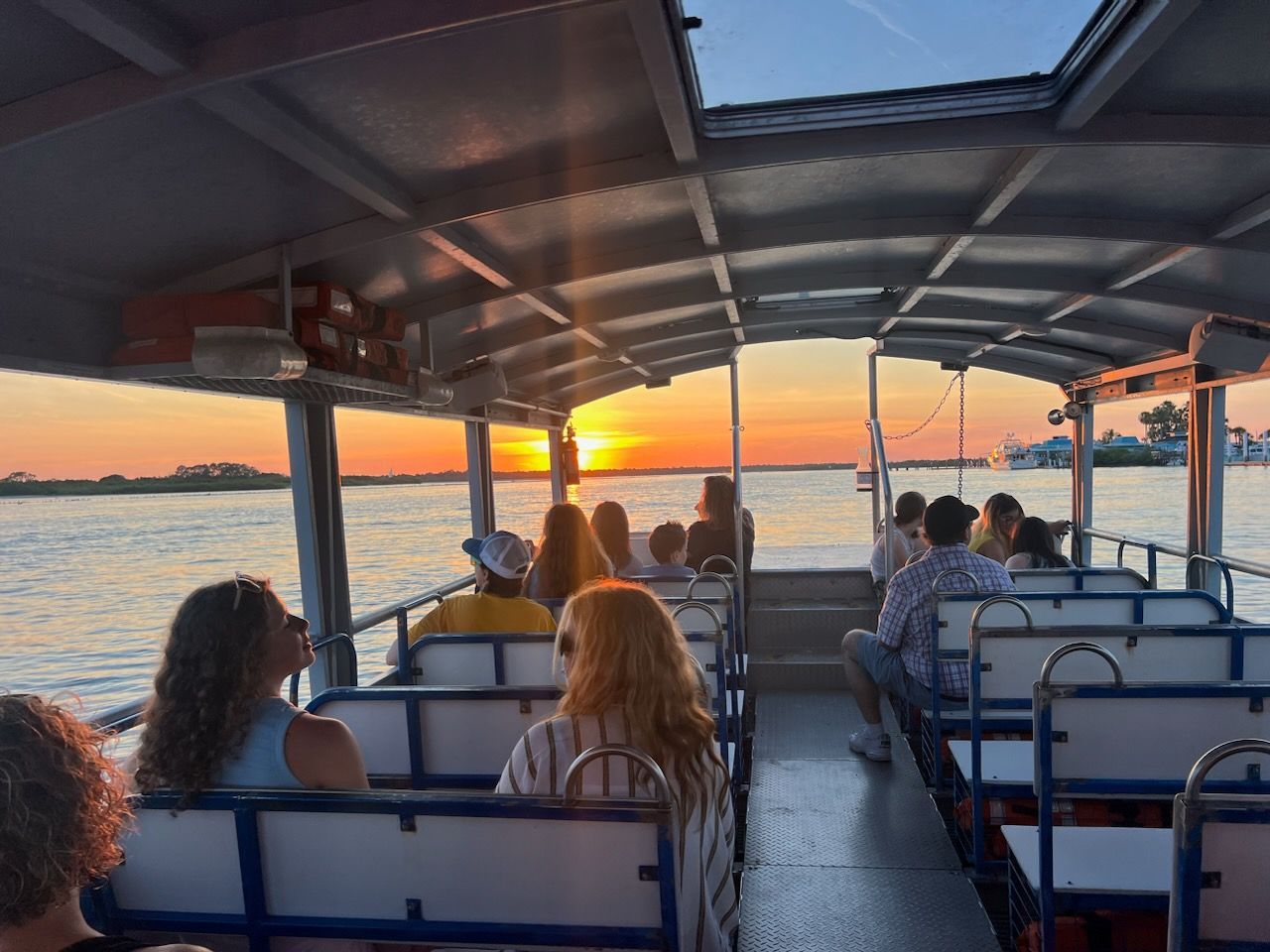 People on a boat watching the sunset over the water. Golden light illuminates the sky and faces.