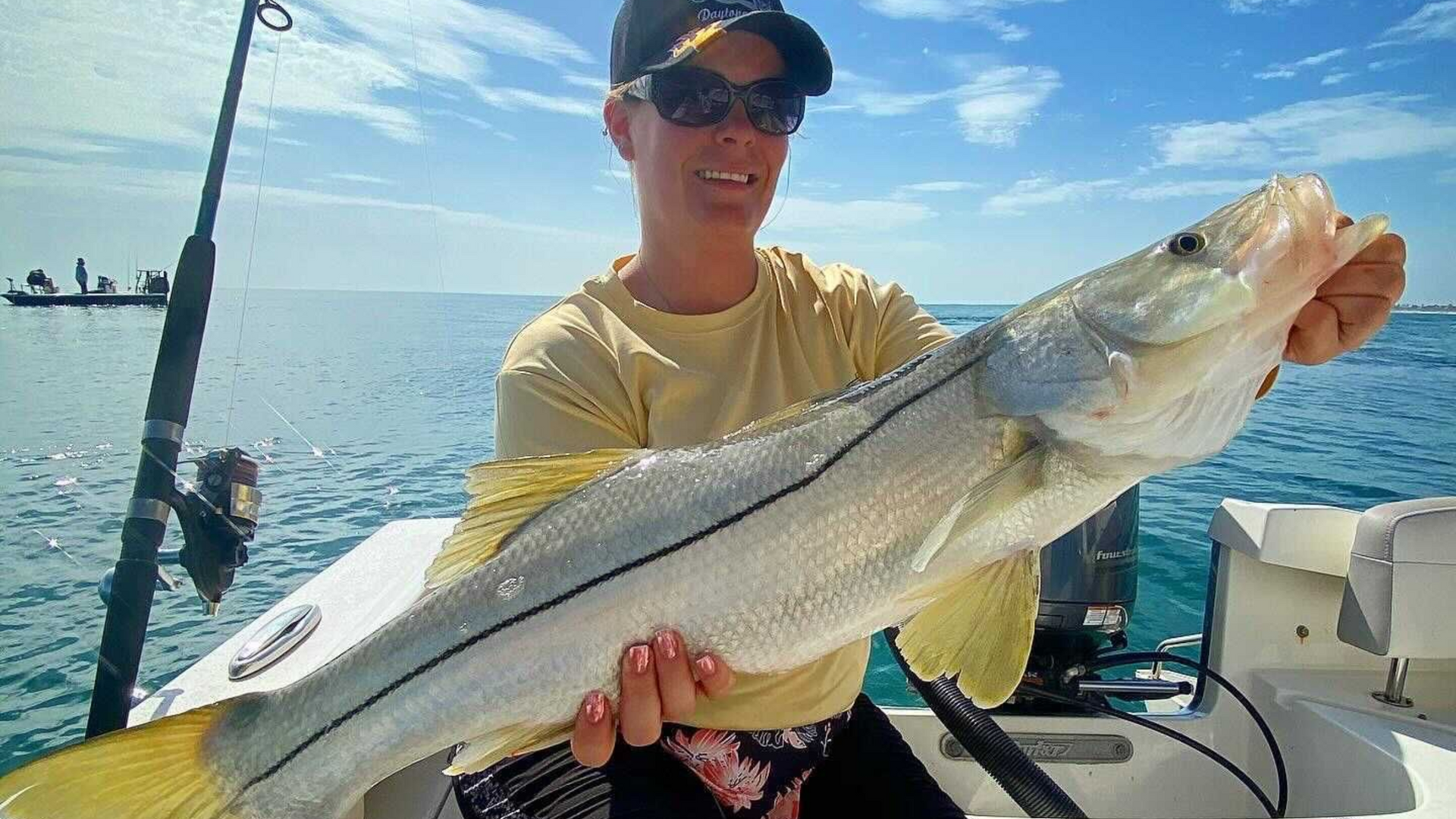 Woman on a boat holding a large silver snook fish, smiling in the sunlight.