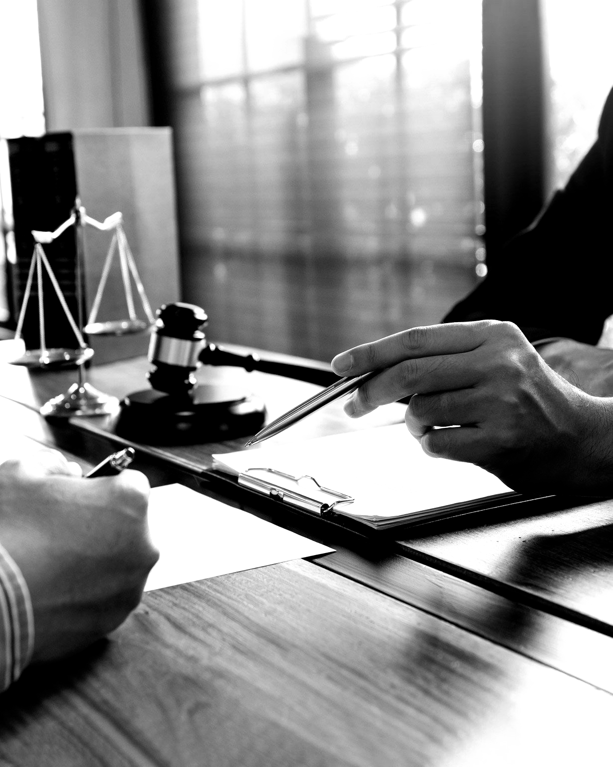 A black and white photo of two people sitting at a table with a judge 's gavel and scales of justice.