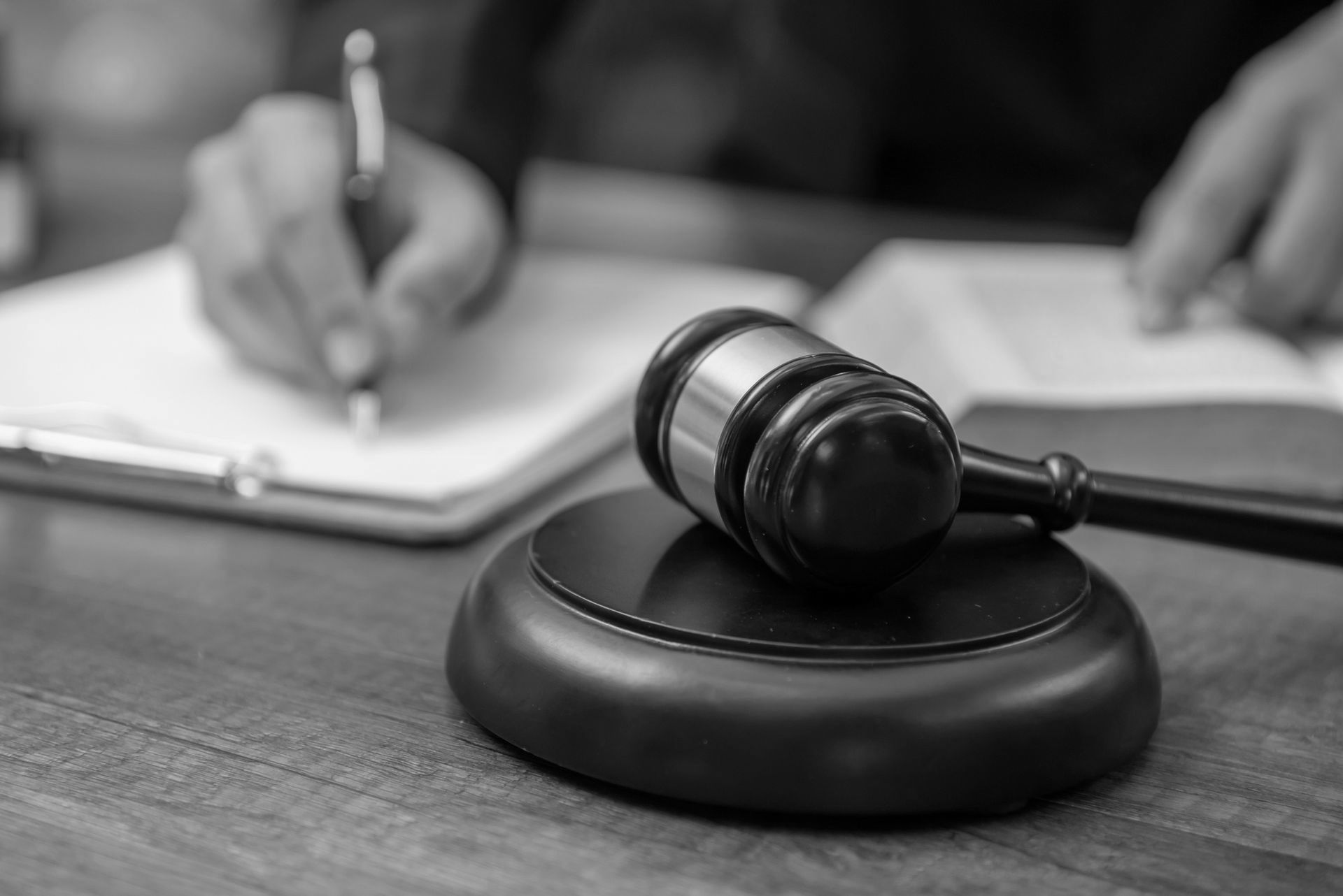 A judge 's gavel is sitting on a wooden table next to a person writing on a clipboard.