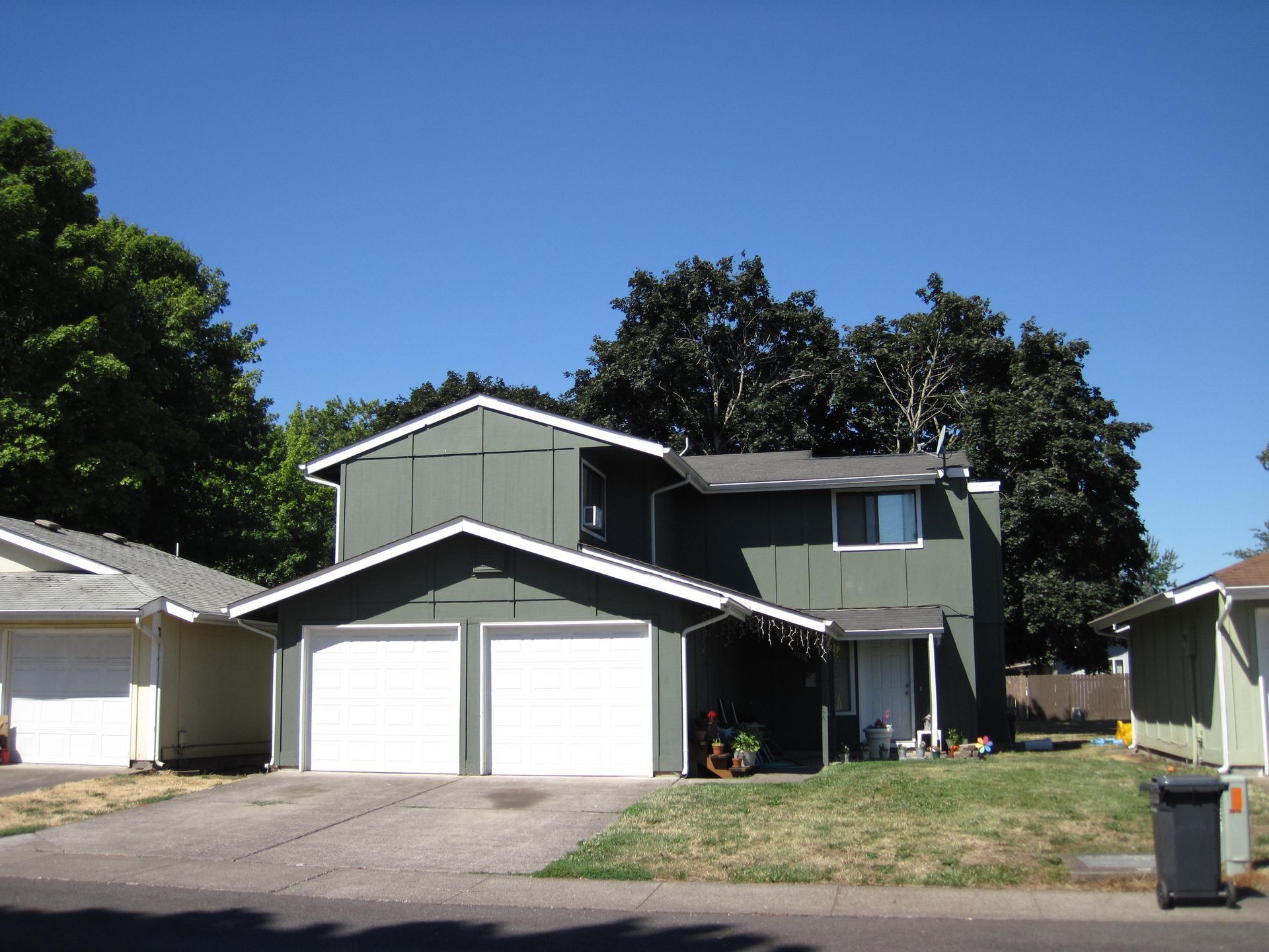 Two-story green house with white garage doors, driveway, and a clear blue sky.